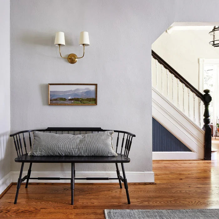 Two-shade wall light above a framed landscape and black hallway bench.