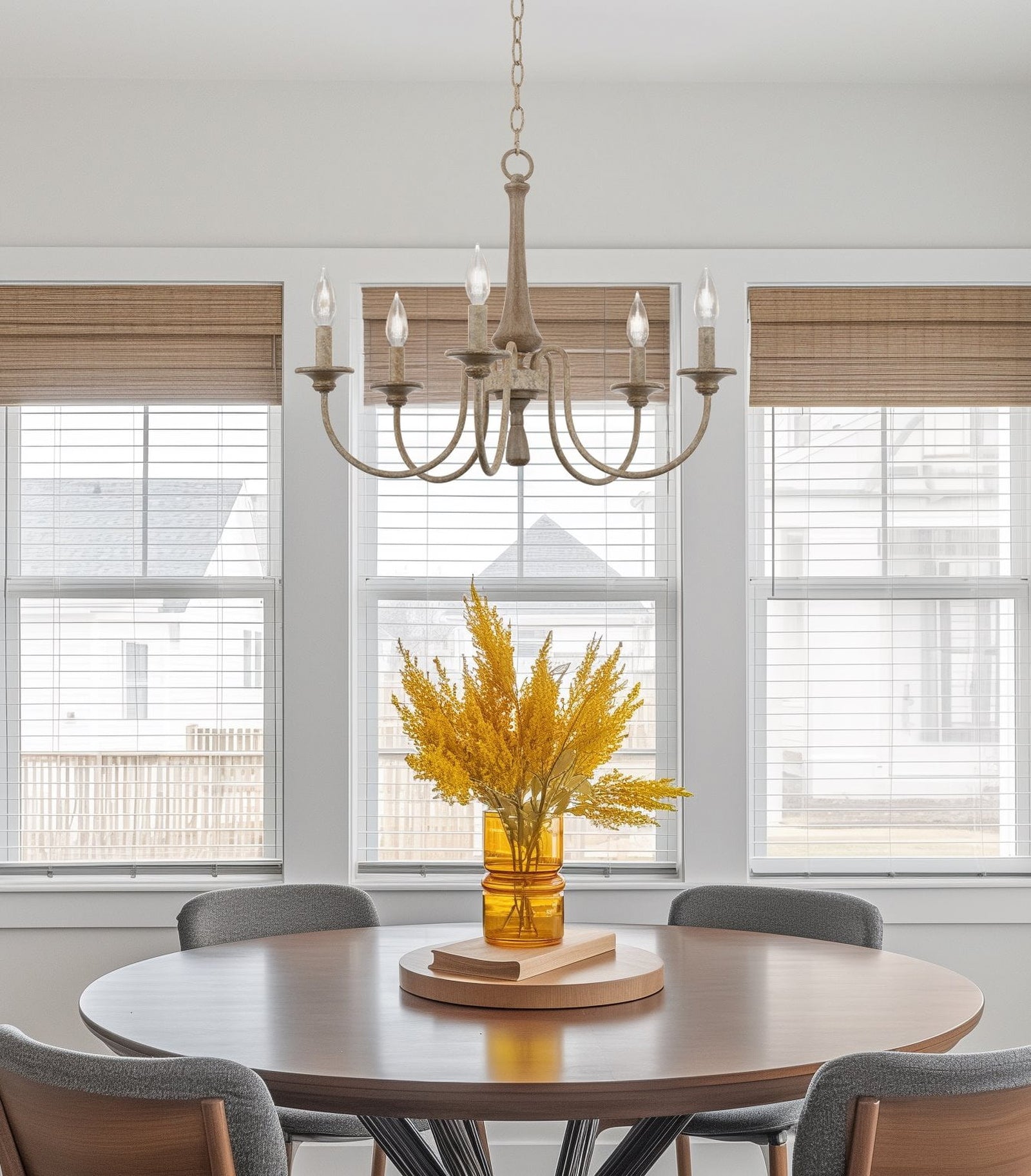 Pale five-light chandelier above a round wooden dining table with yellow flowers and window blinds