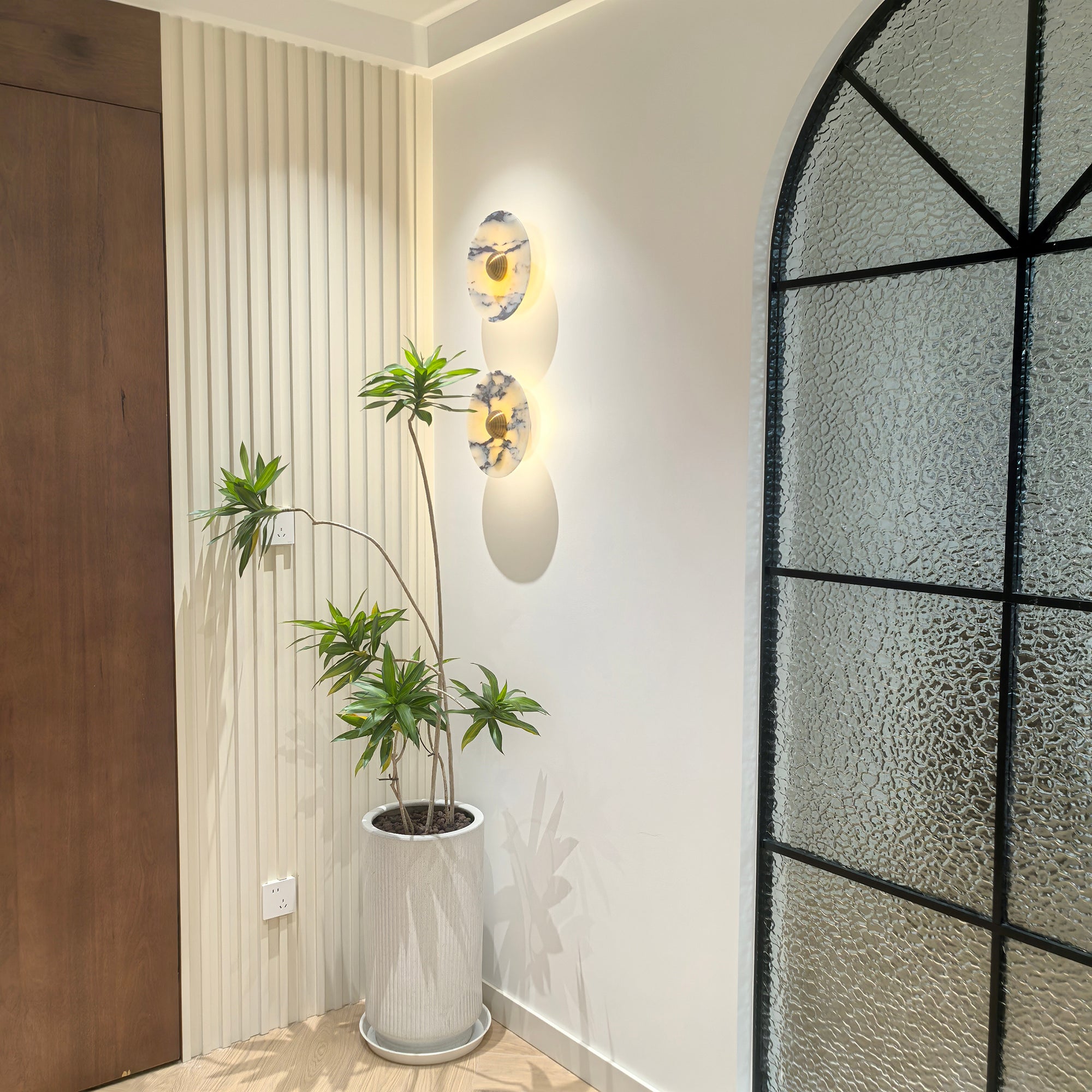 Two glowing Gold-centred stone wall lights beside a tall plant and an arched textured-glass partition