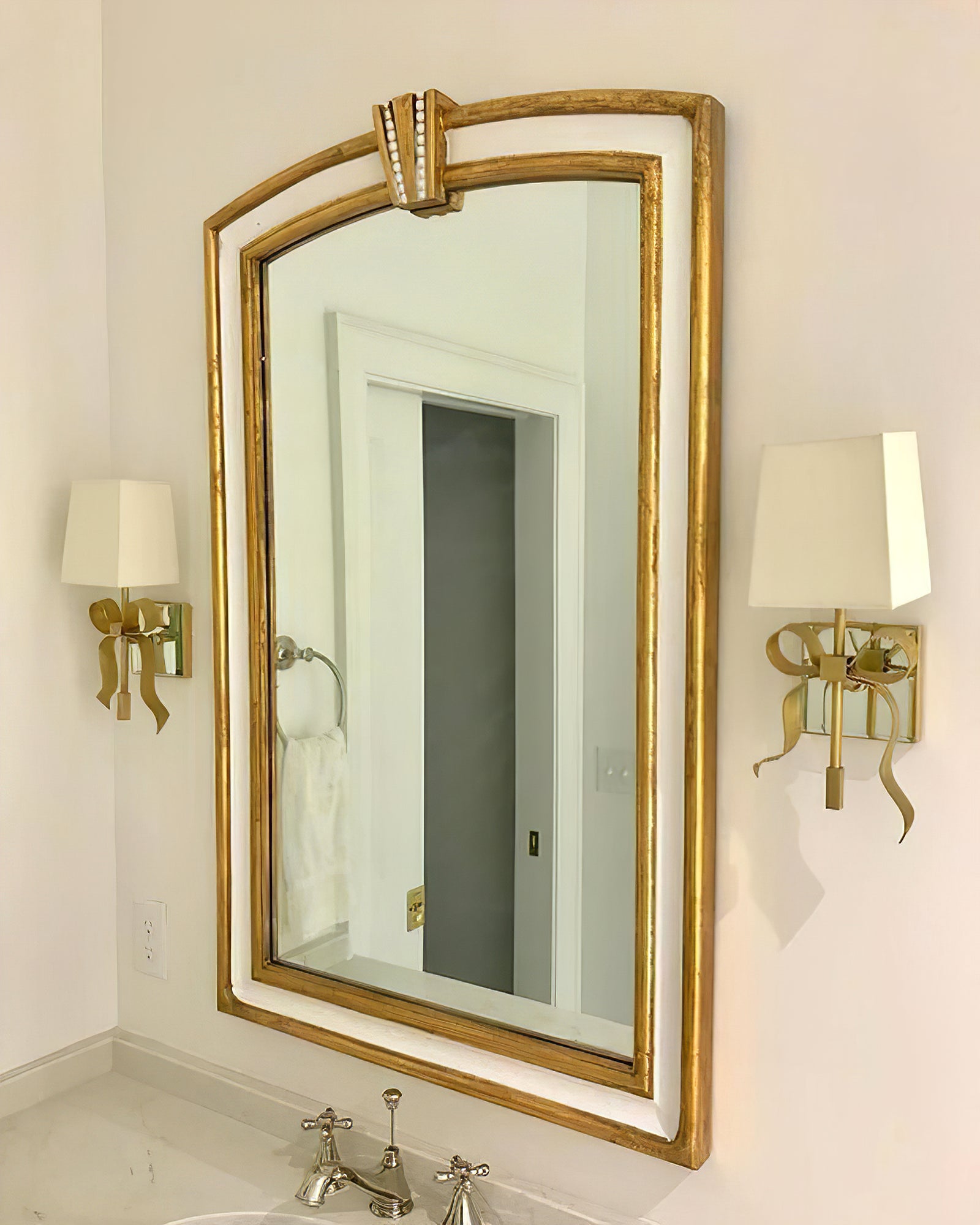 Brass-tone bow lights with pale tapered shades on each side of a tall gold-framed mirror