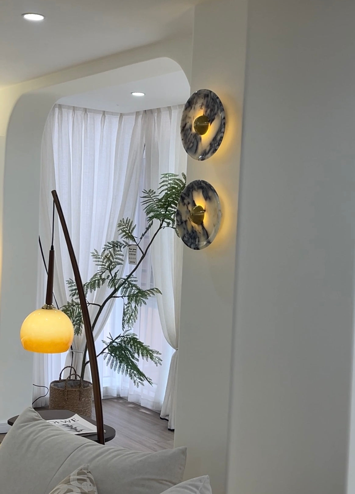 Angled view of two Gold-centred veined wall lights glowing on a column by curtains and a separate floor lamp