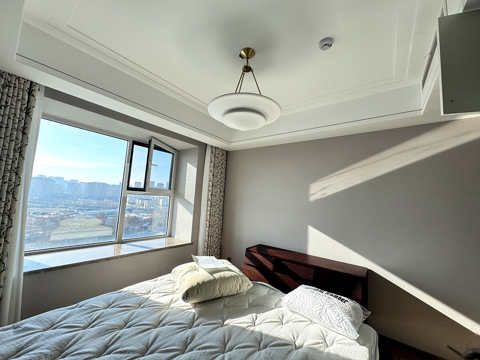 Mollino white tiered chandelier with gold-tone supports and short chain above bed beside large daylight window