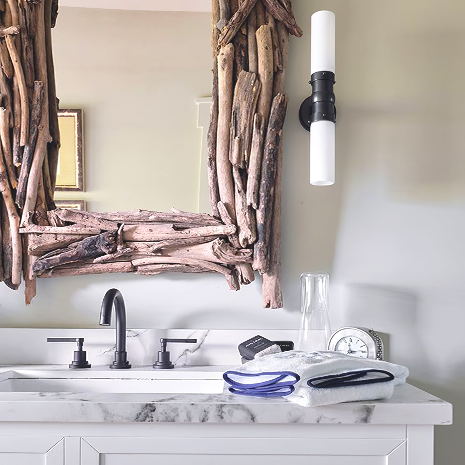 Antique Black double white-glass wall light beside a twig-framed mirror above a counter with towels and a clock