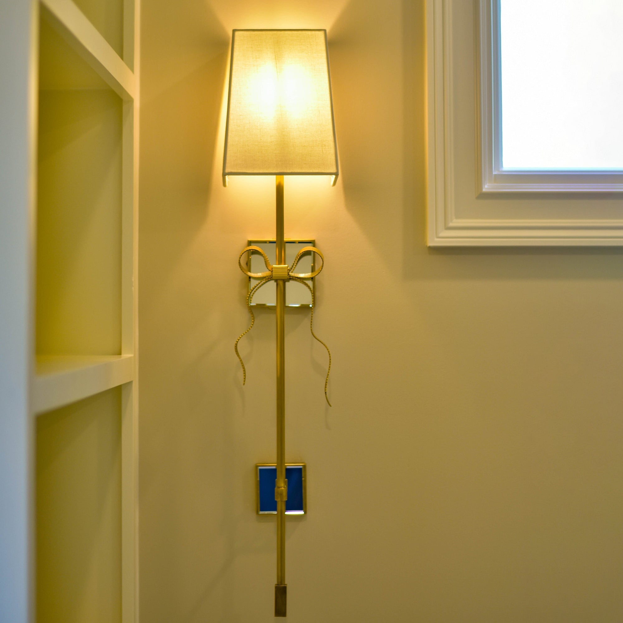 Illuminated white Ellery shade and gold bow against a yellow-toned wall