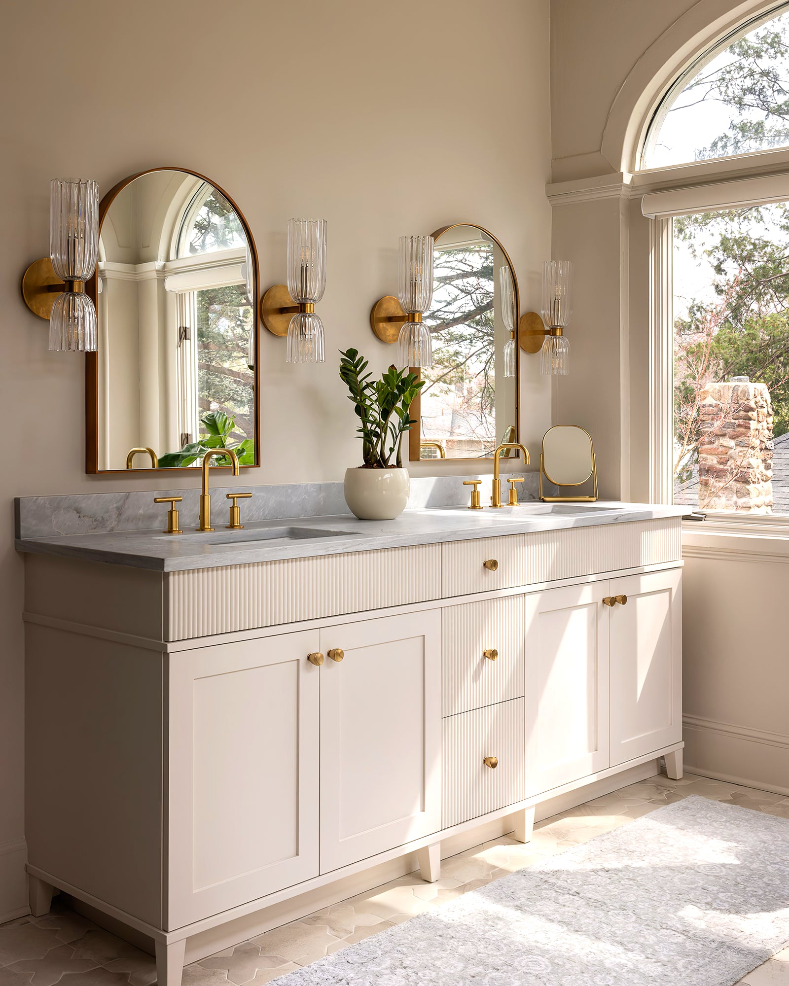 Four double glass wall sconces arranged around two arched mirrors above a large white double vanity