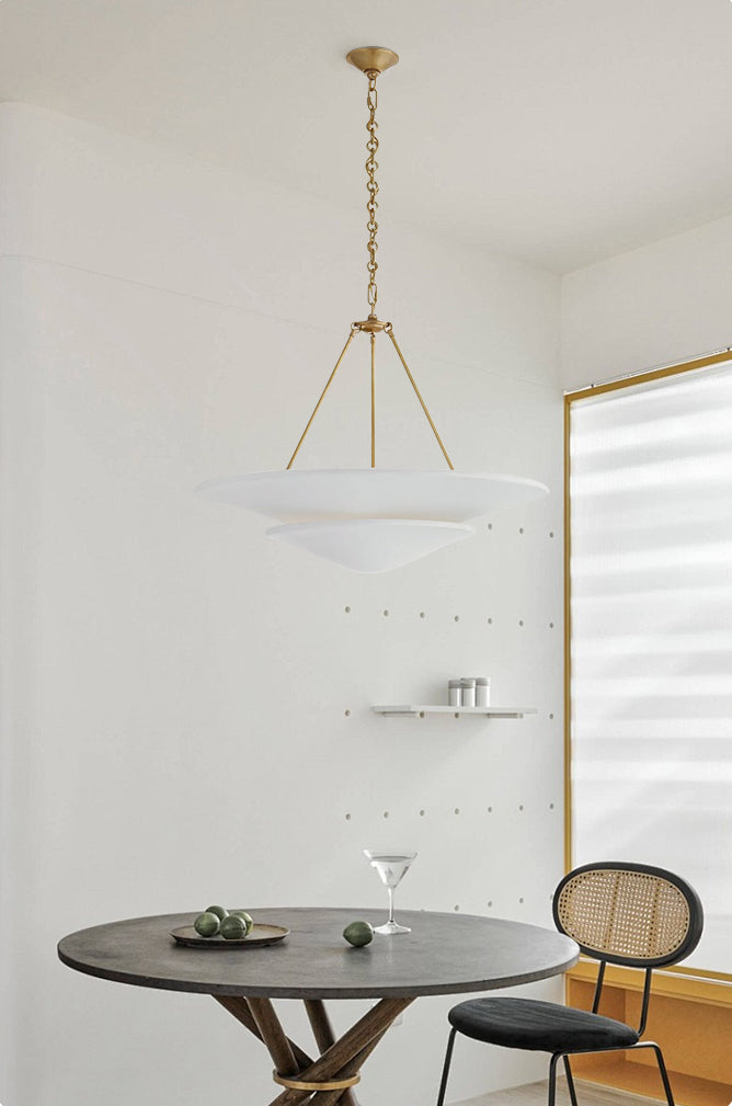 White Mollino tiered chandelier with gold-tone chain above round dining table with fruit and cane-backed chair