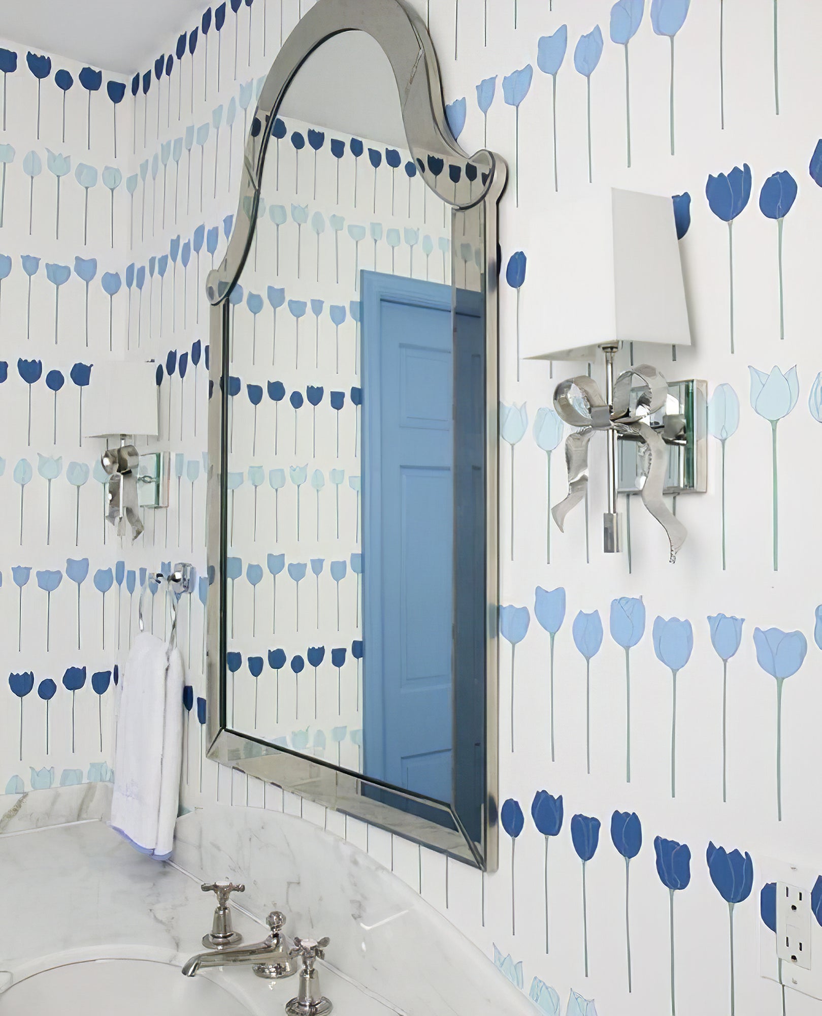 Silver-tone bow lights with pale rectangular shades beside a shaped mirror on blue tulip wallpaper