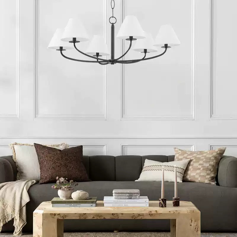 Six-light Black Stacey chandelier with white shades above grey sofa and coffee table with books and candles