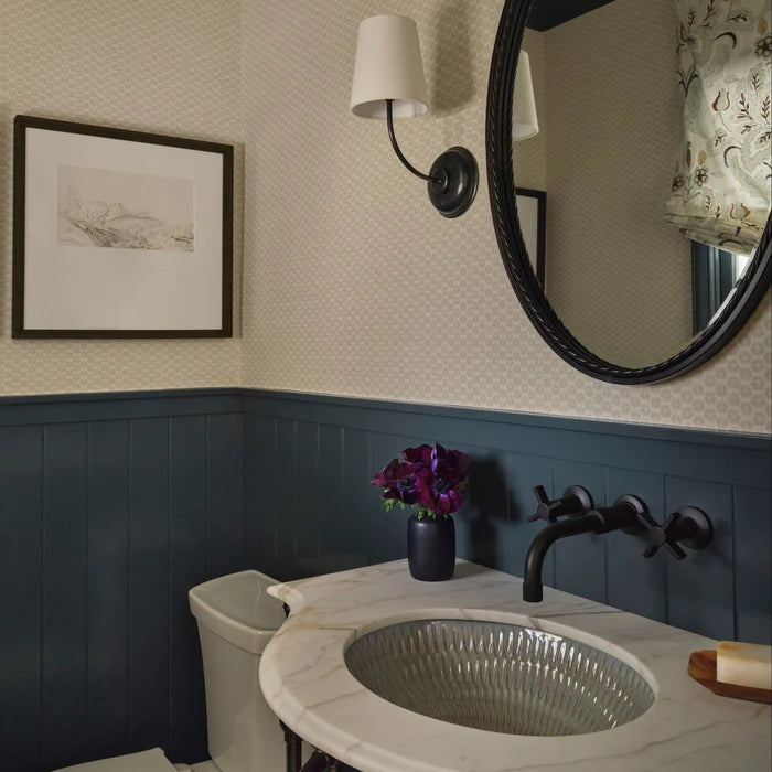 Black single-shade wall light beside a round mirror and washbasin.