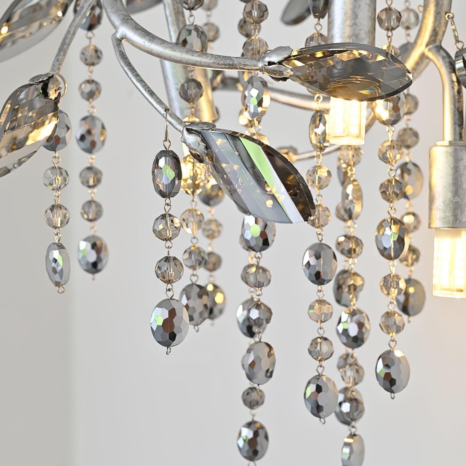 Close-up of silver-tone branches, faceted leaf ornaments, oval bead strands and glowing cylindrical lamps