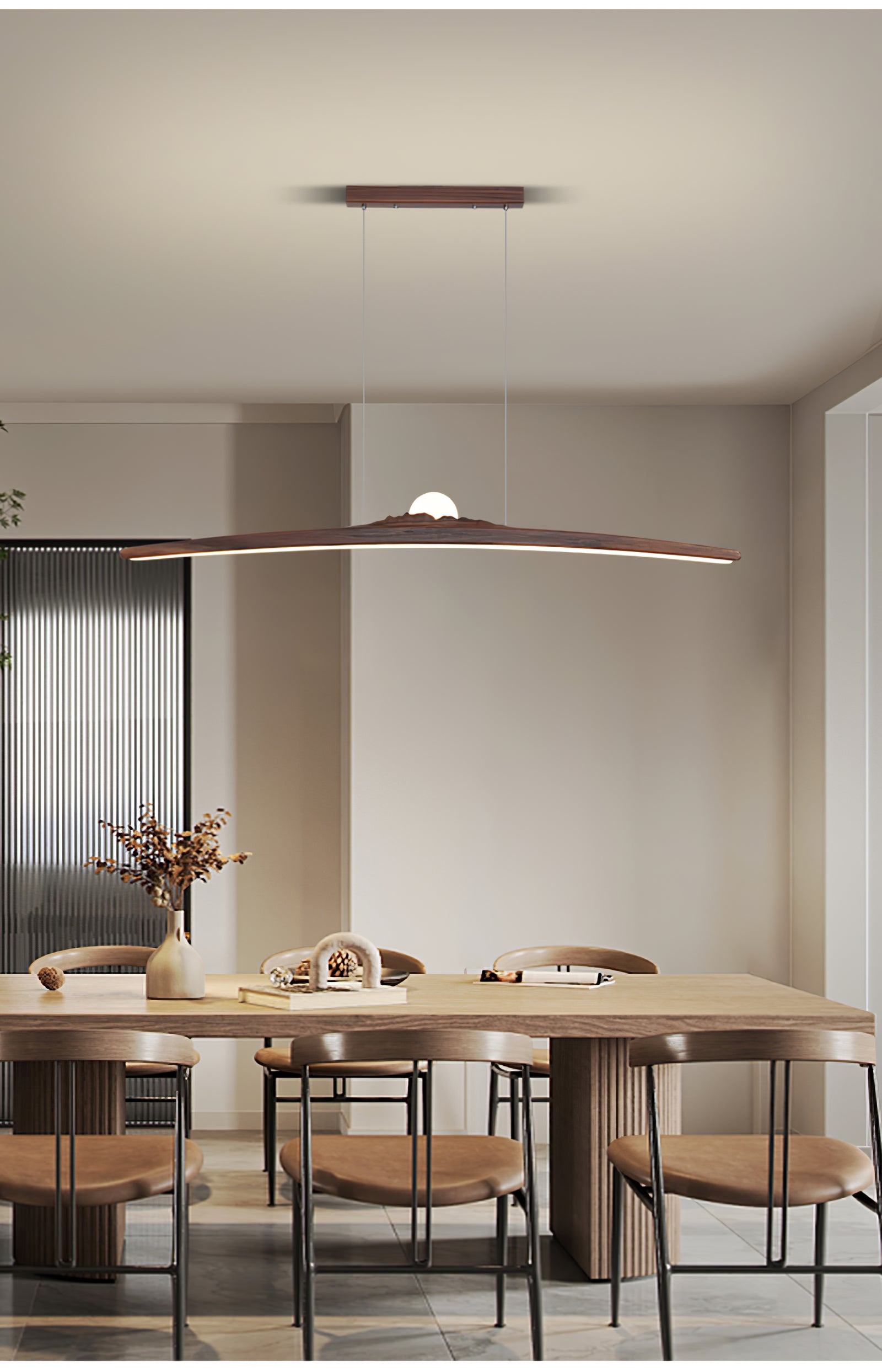 Dark curved wood pendant above a long timber dining table with chairs, a vase and a book
