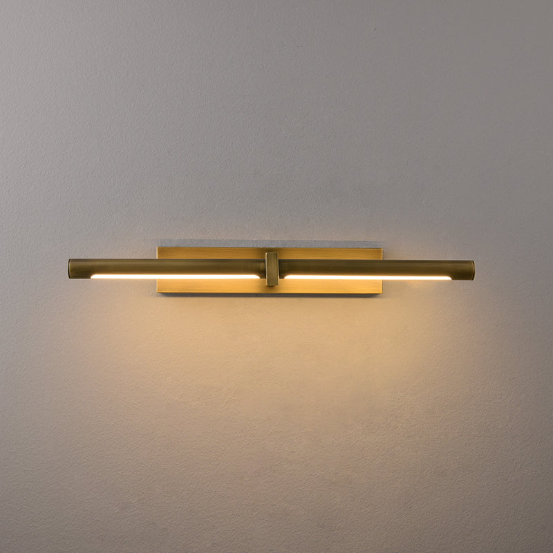 Front view of lit brass-colour cylindrical picture light and rectangular backplate on a pale wall