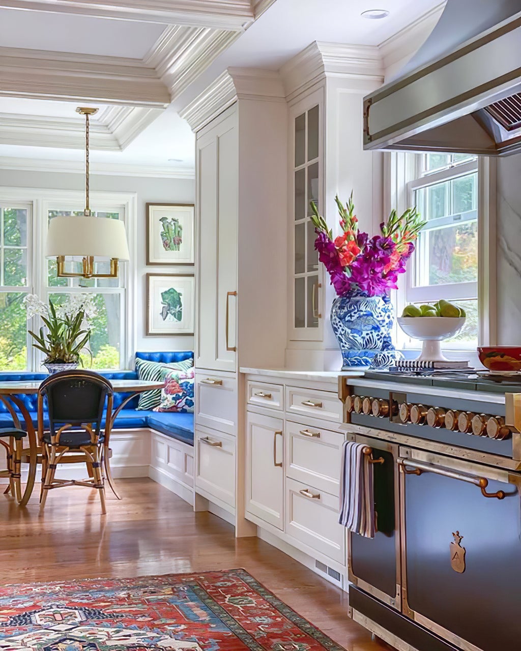 Gold-toned shaded chandelier over a blue breakfast banquette, with blue cooker and flowers in foreground
