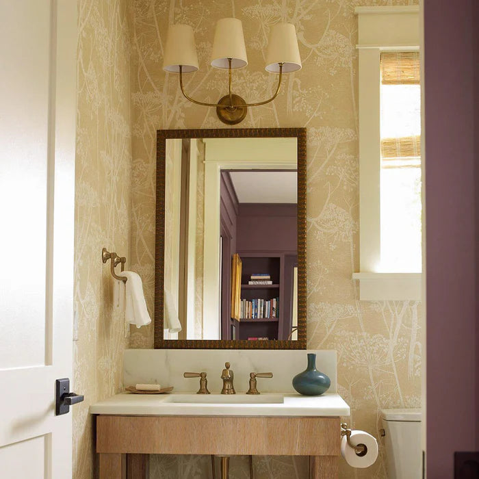 Three-shade brass wall light above a rectangular mirror and small basin.