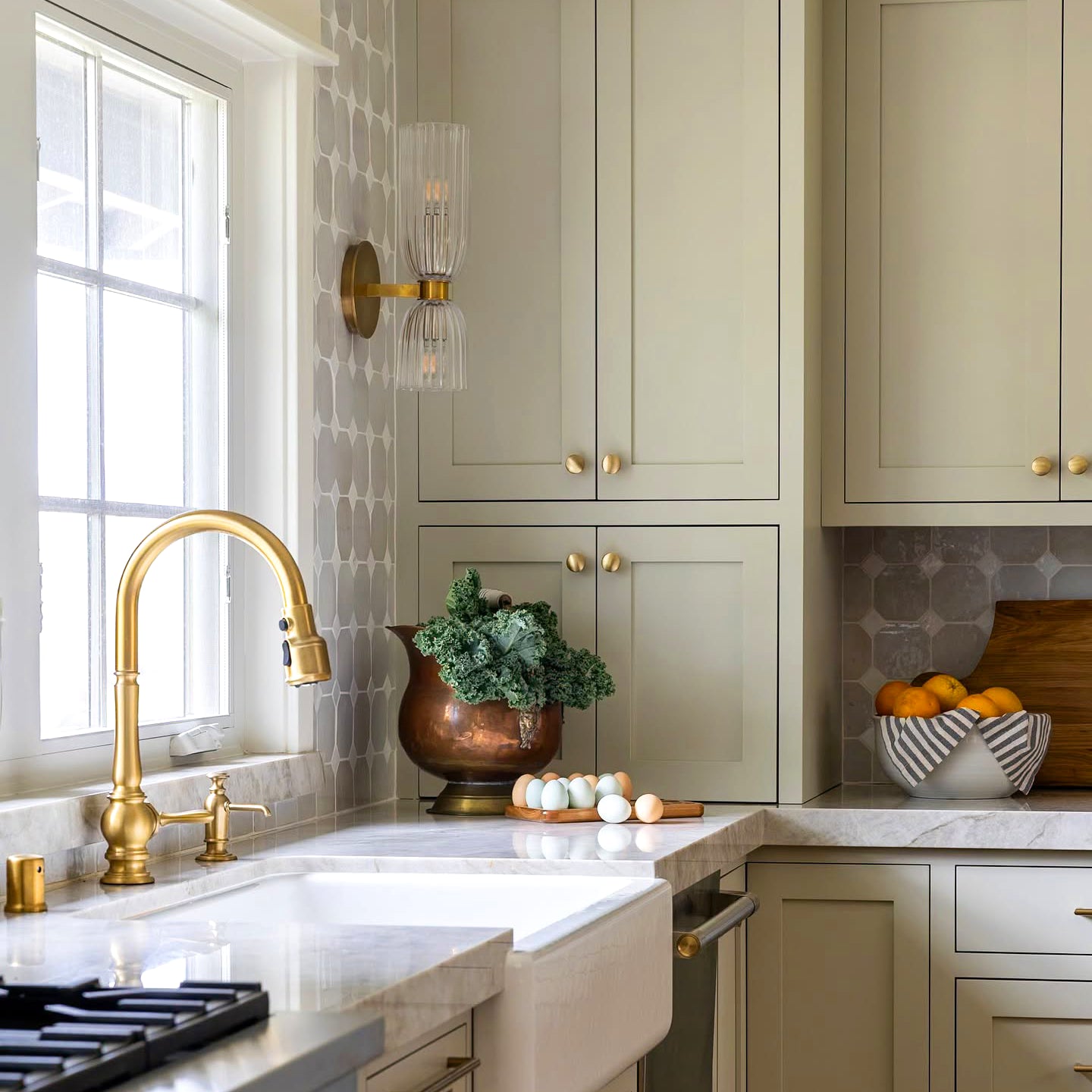 Antique Brass-tone double glass wall sconce by a kitchen window and sink with green cabinets