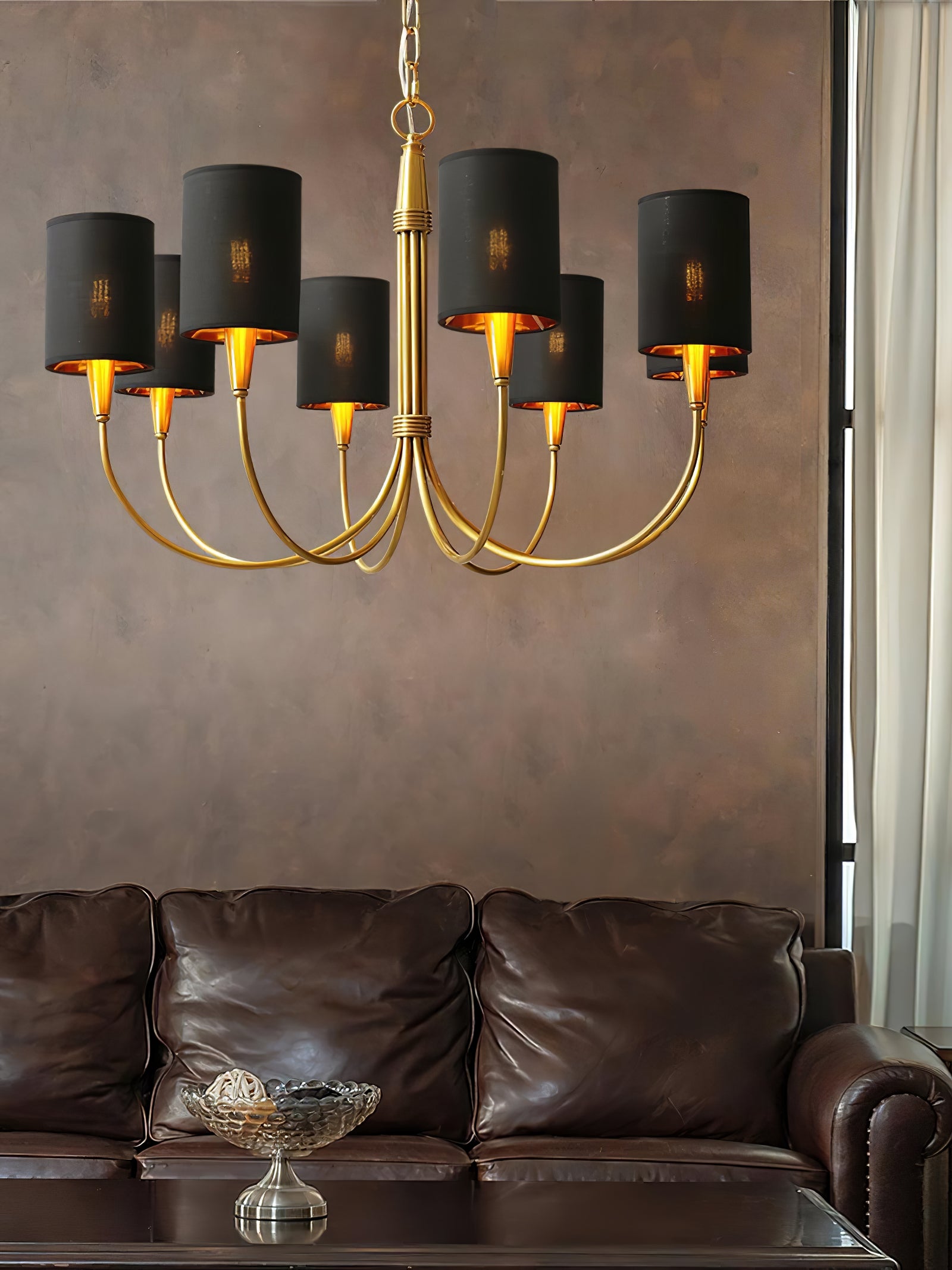 Eight-light Quincy chandelier with black shades and gold-tone curved arms above a brown leather sofa and glass coffee table