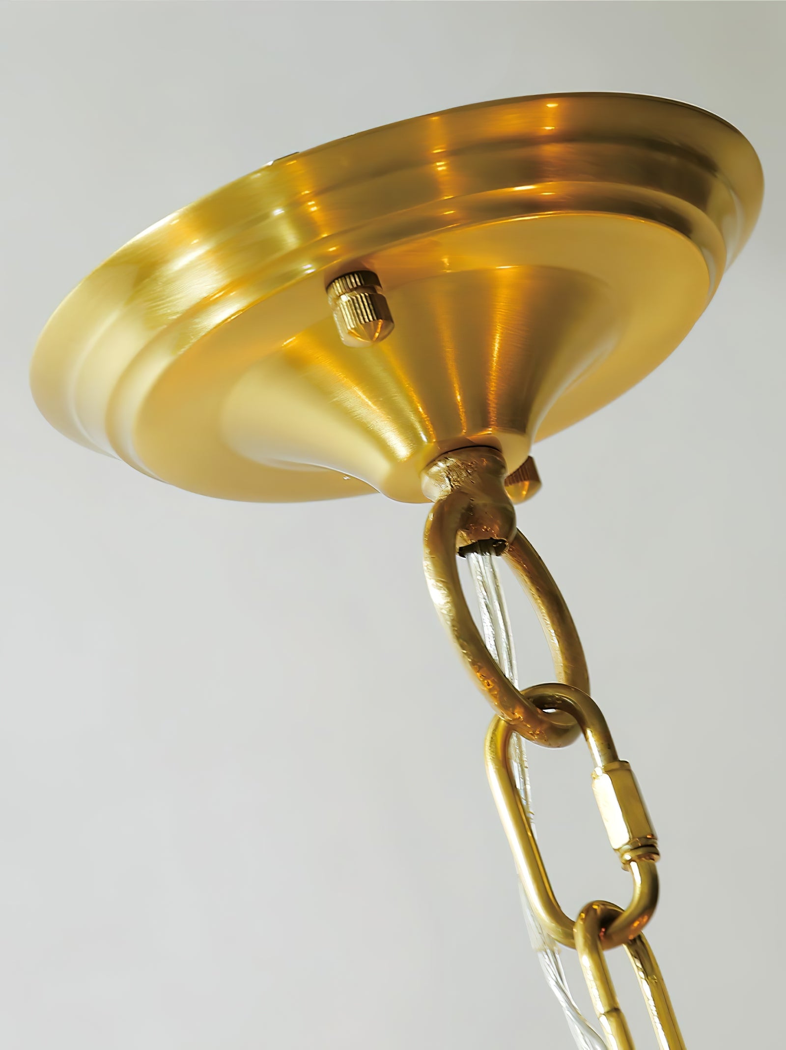 Close view of Quincy gold-tone round stepped canopy, ribbed fixing nuts, chain link and clear cable