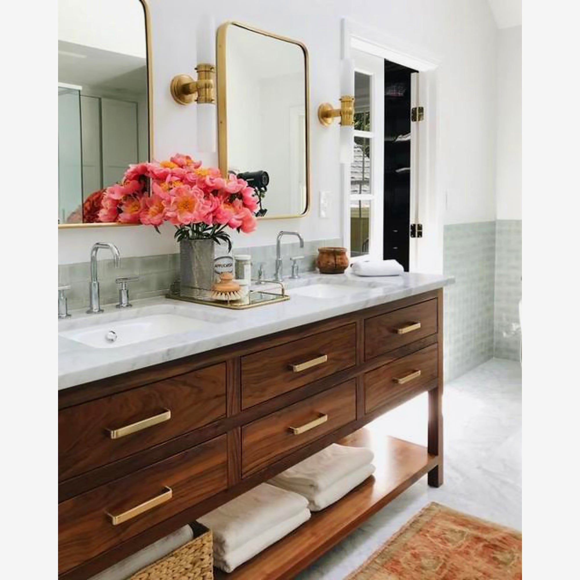Two brass-tone double wall lights by gold-trimmed mirrors above a wood vanity with pink flowers