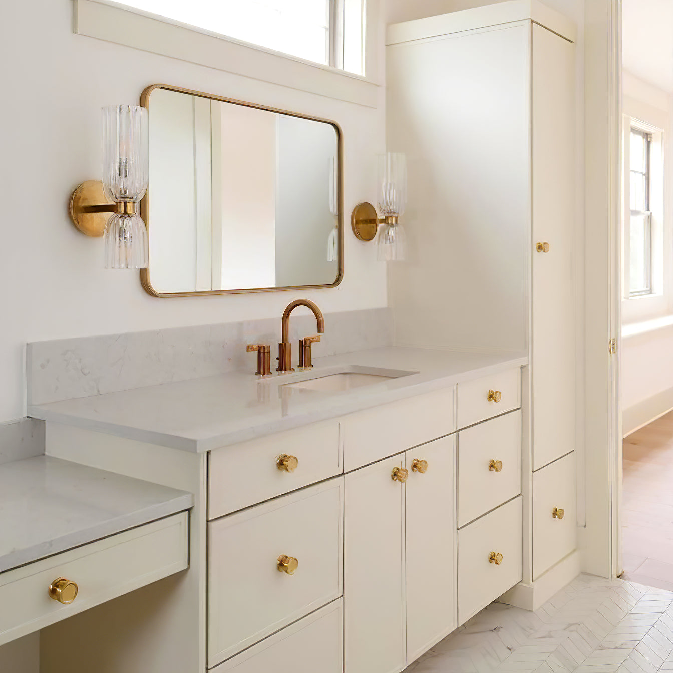 Pair of double ribbed glass sconces around a gold-framed horizontal mirror above a white vanity
