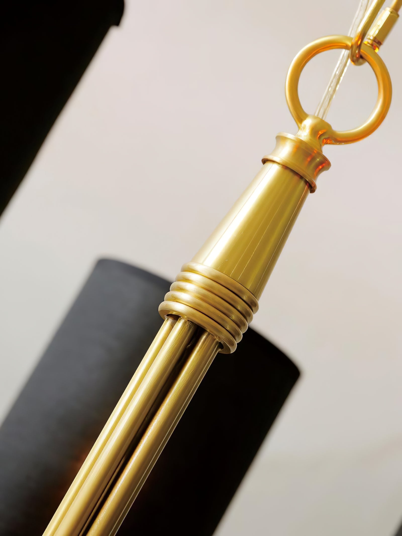 Close view of Quincy gold-tone fluted central stem, decorative rings, suspension chain and cable with black shade behind