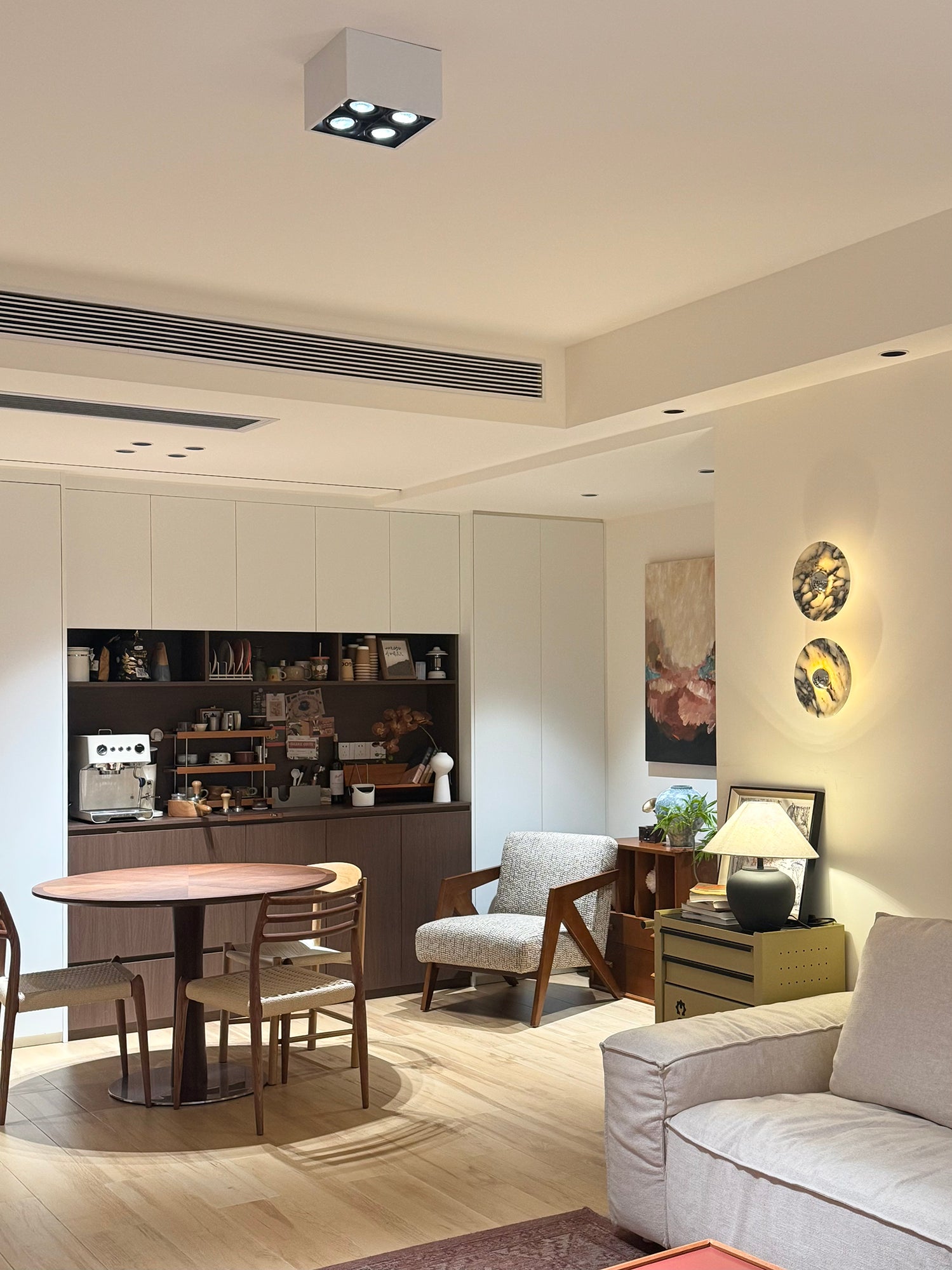 Two glowing stone wall lights above a lamp cabinet beside an indoor dining area and coffee-machine shelves