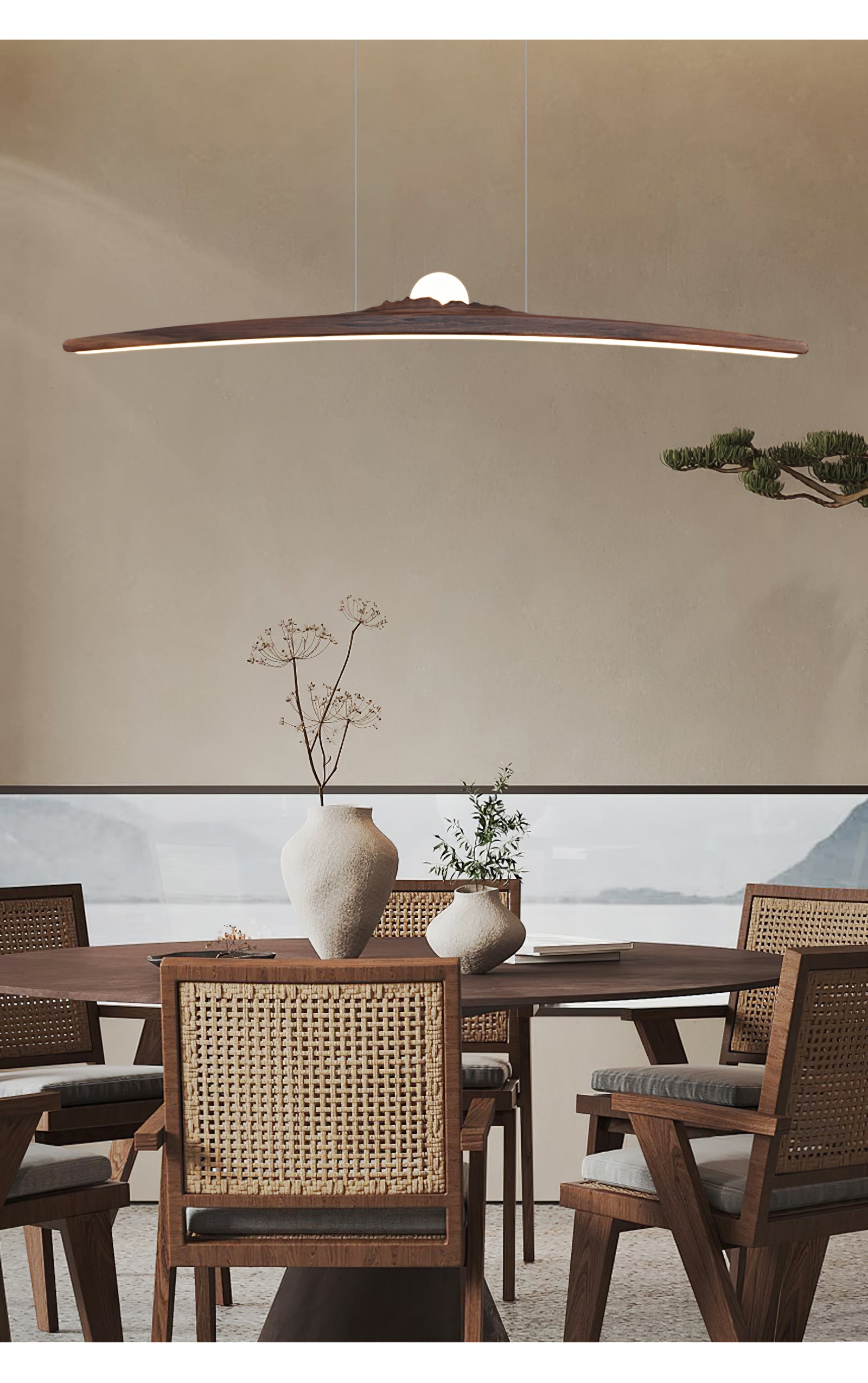 Dark curved pendant over a timber dining table with vases and woven chairs by a window