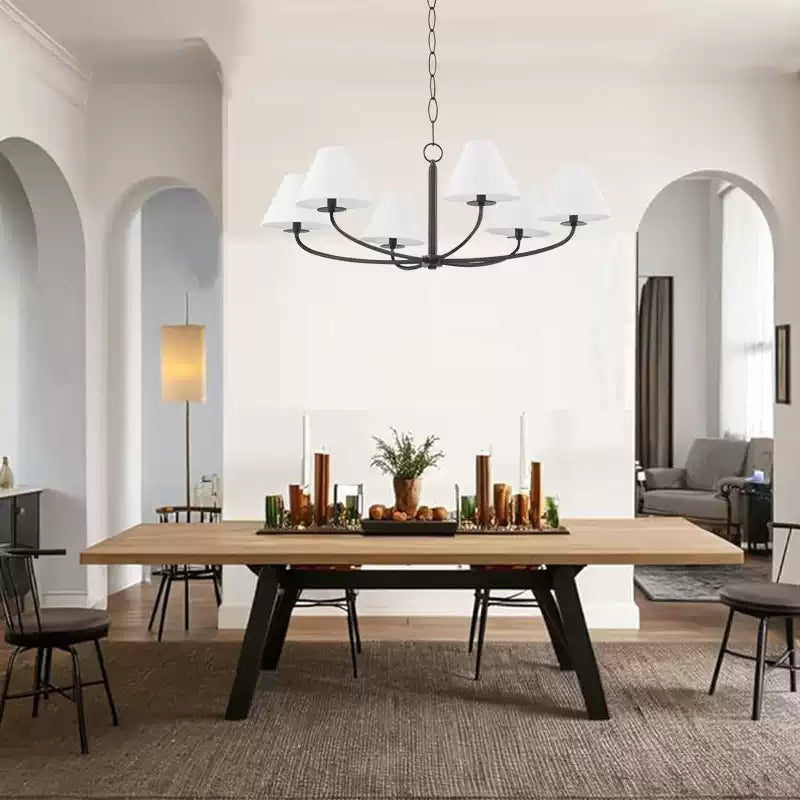Stacey black curved-arm chandelier with white shades over rectangular dining table with candles before arched openings