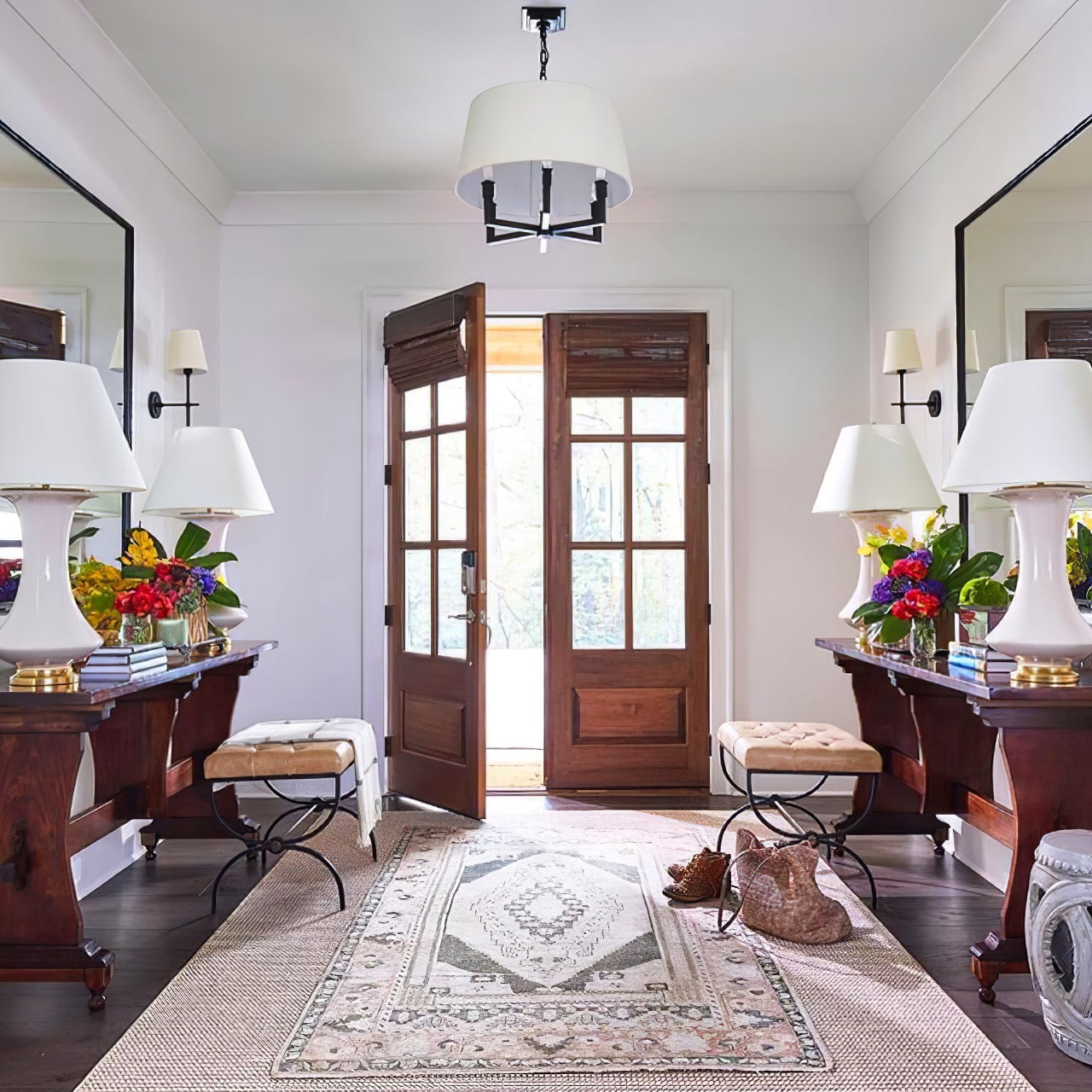 Black framed shaded chandelier in an entrance hall with wooden double doors, mirrored consoles and benches