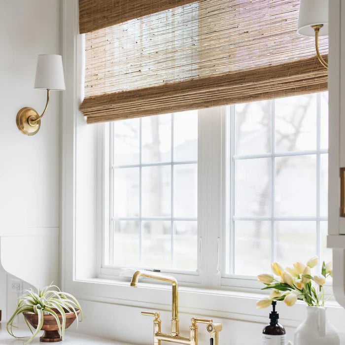 Brass single wall light beside a kitchen window with a woven blind.