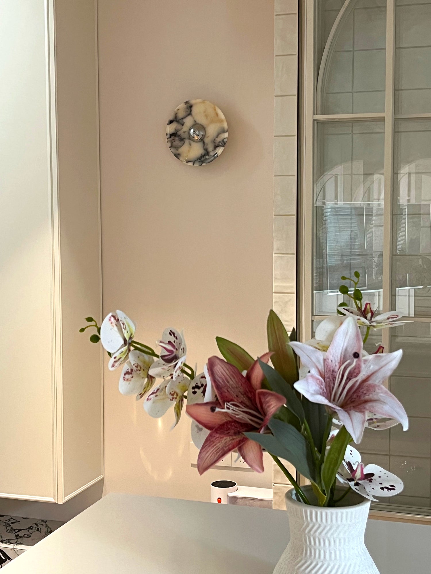 Single Silver-centred stone wall light above a white counter behind a vase of lilies