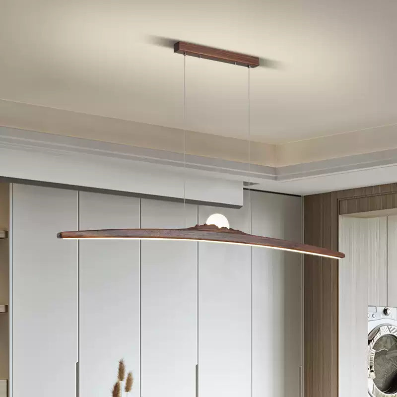 Dark curved wood pendant with a glowing globe and luminous underside above pale cabinets