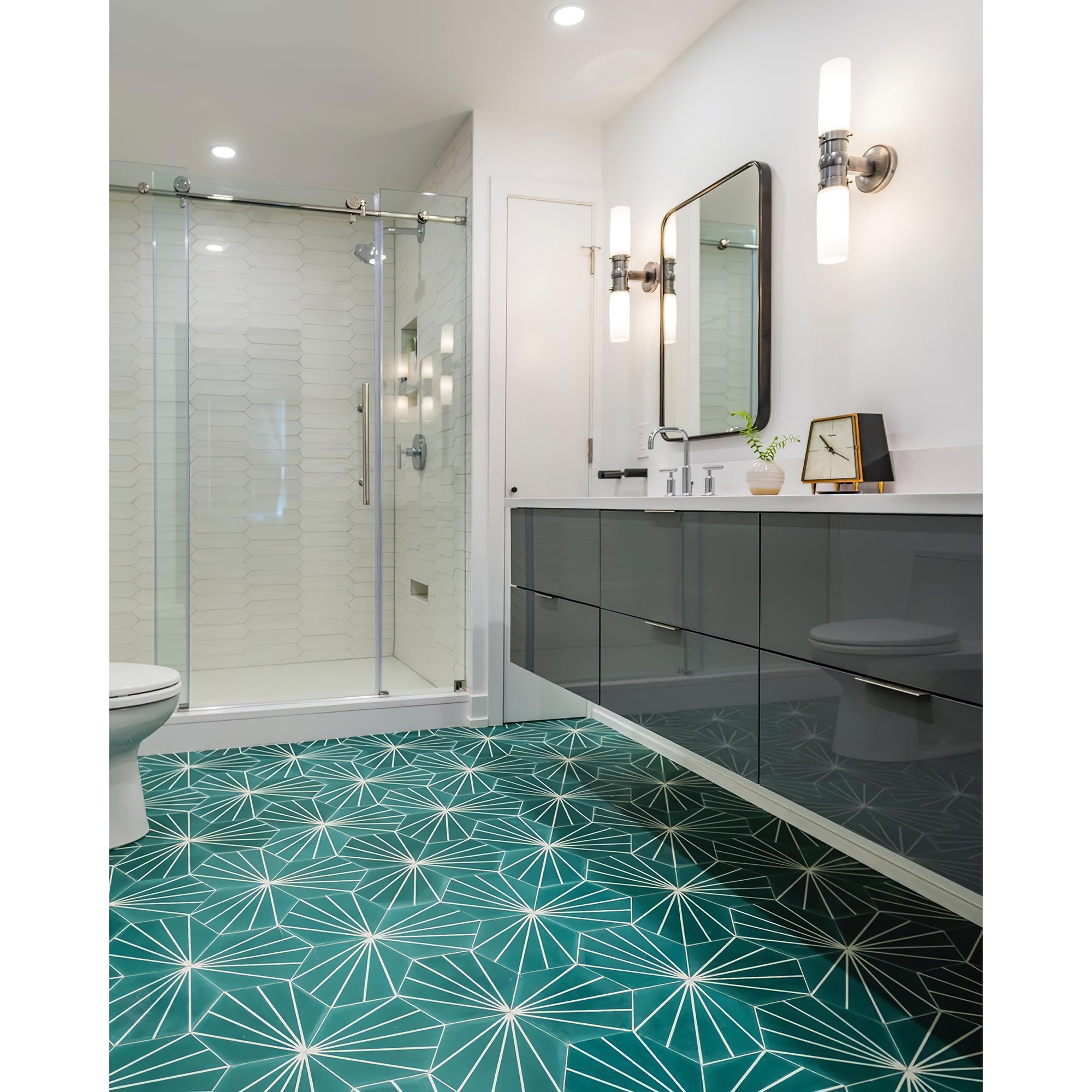 Two glowing silver-tone double glass wall lights beside a black-framed mirror near a hexagon-tiled shower