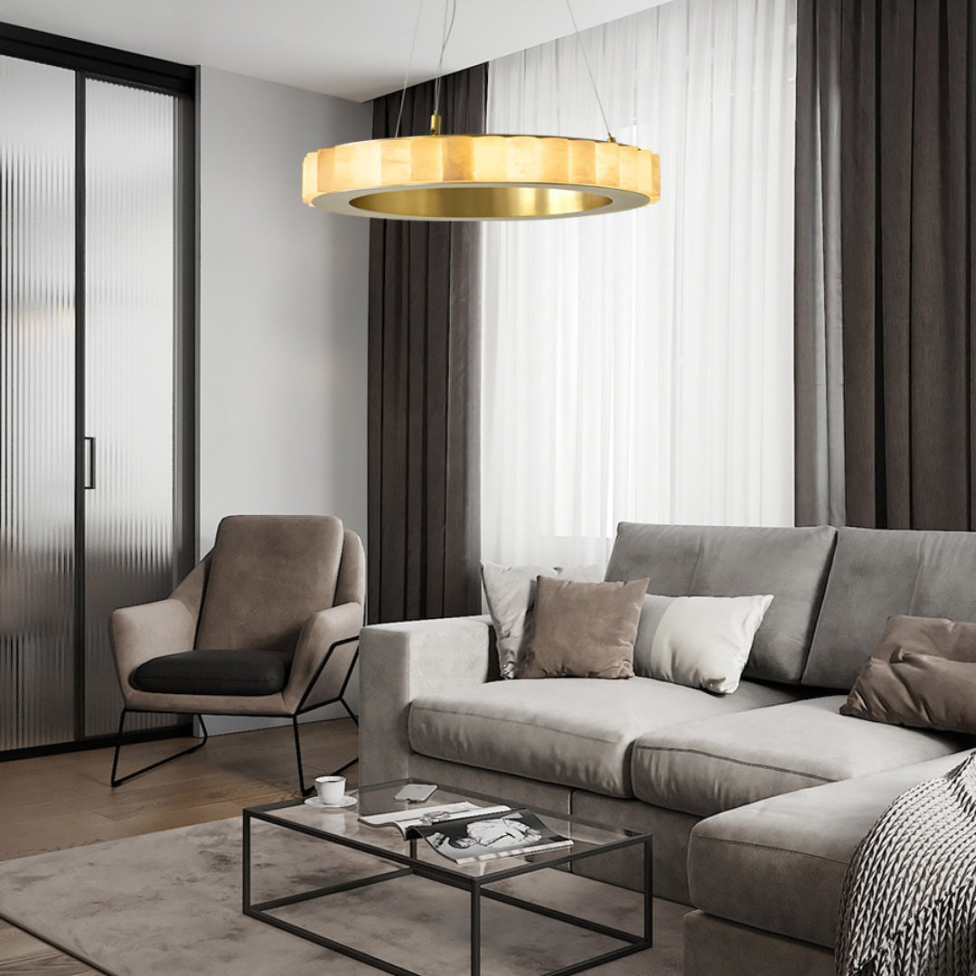 Gold-tone ring chandelier with pale glowing segments above a grey sofa and coffee table