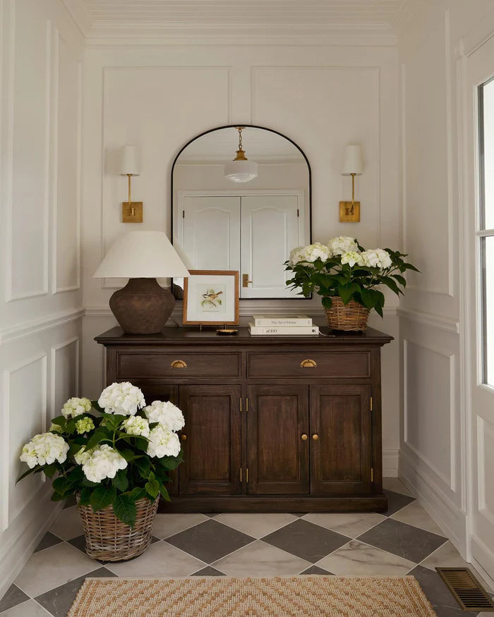 Two brass single wall lights flanking an arched mirror above a wooden vanity.