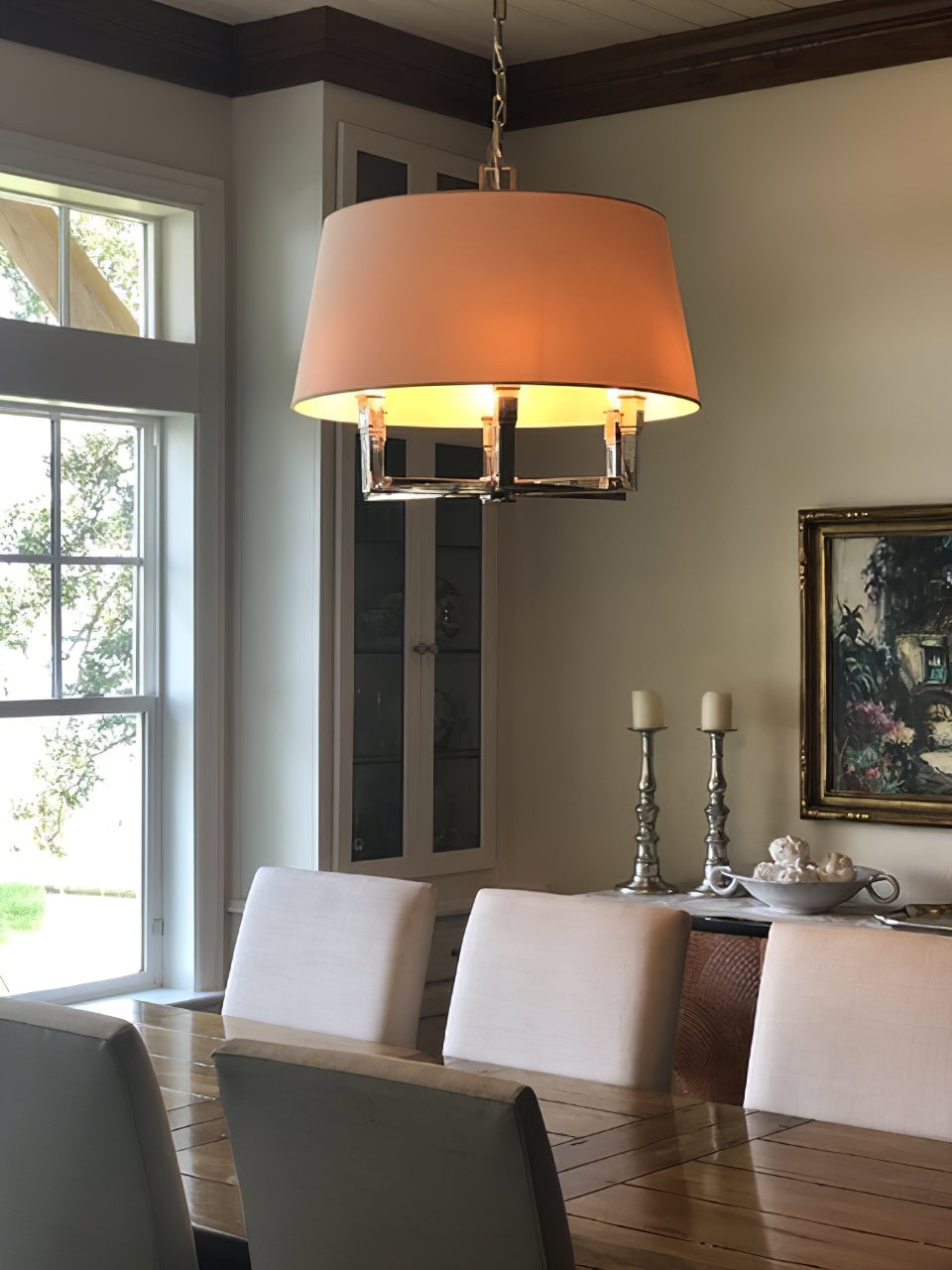 Illuminated tan-looking chandelier shade above a wooden dining table with grey upholstered chairs and sideboard