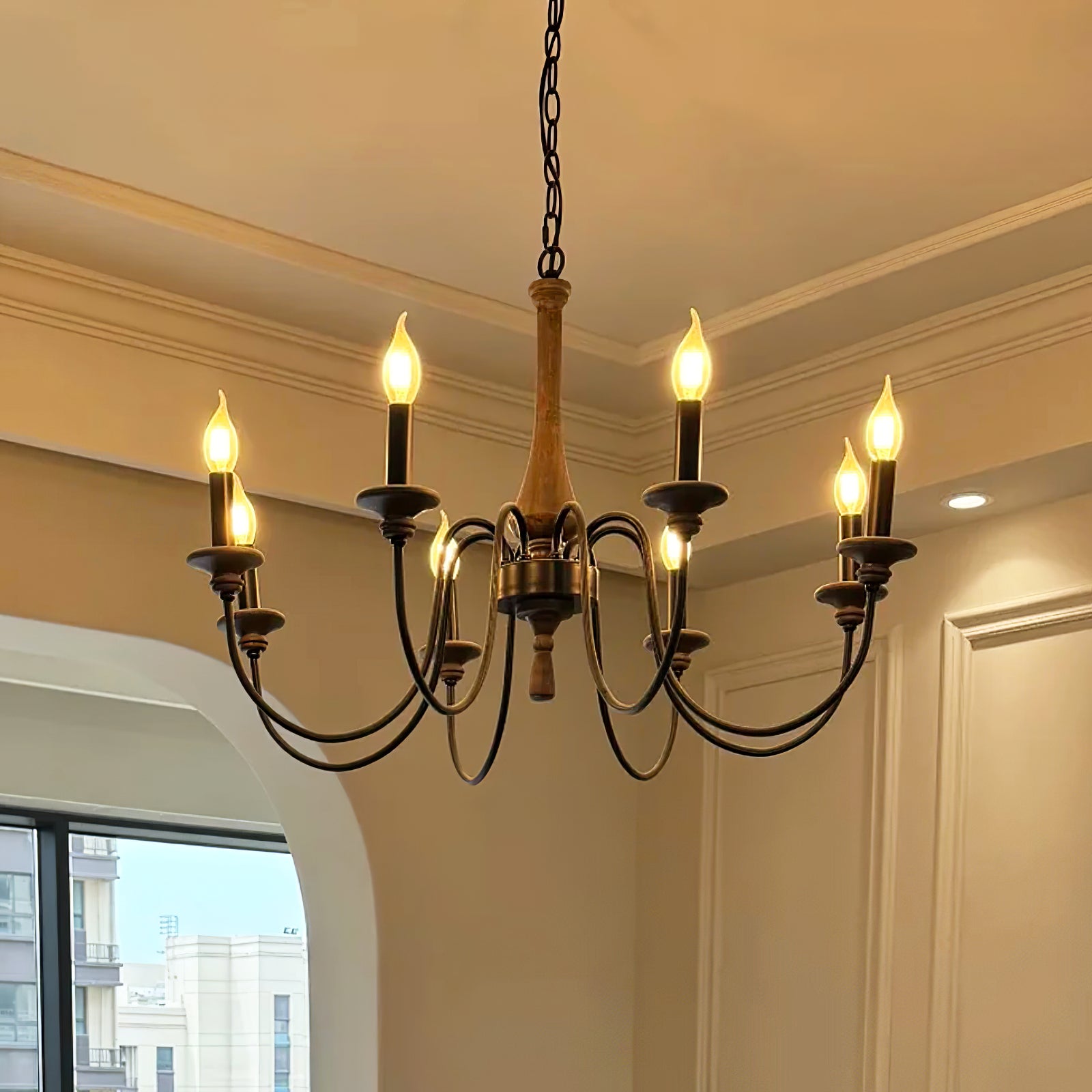 Lit eight-light wood-toned chandelier with black curved arms near a window and moulded ceiling