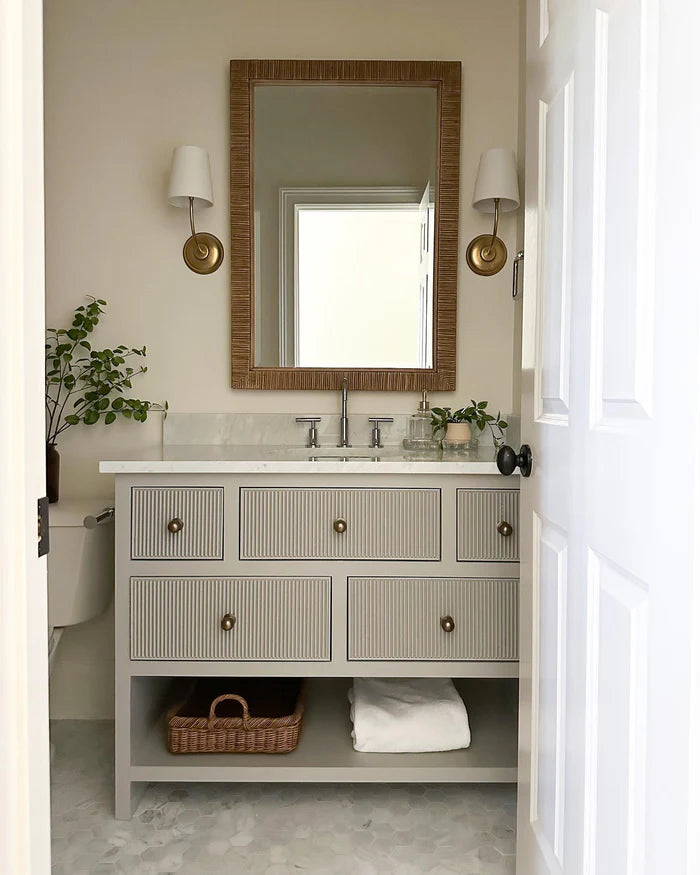 Round-backplate brass single wall lights beside a rectangular vanity mirror.