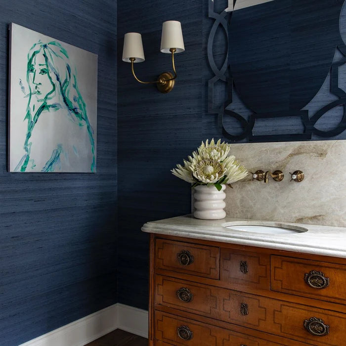 Brass double wall light on a dark blue wall above a wooden vanity.