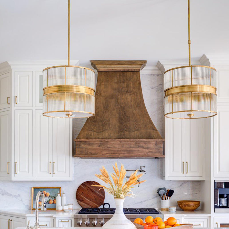 Bronze-tone glass-rod drum pendants beside a wooden range hood in a white kitchen
