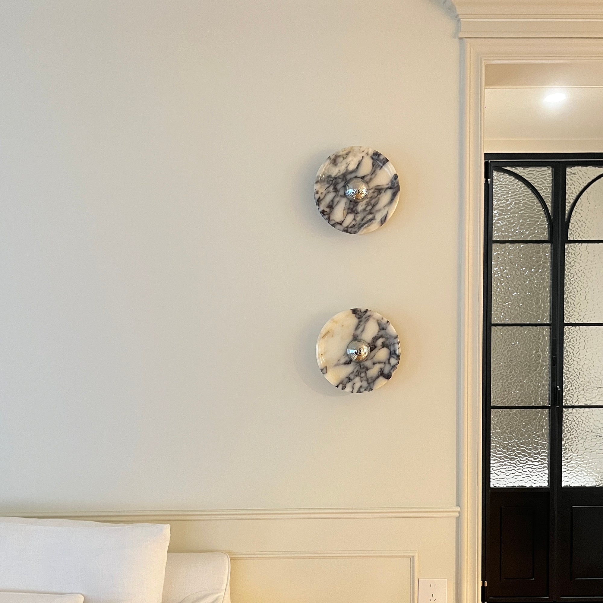 Close view of two Silver-centred veined stone discs on a panelled wall by a textured-glass door