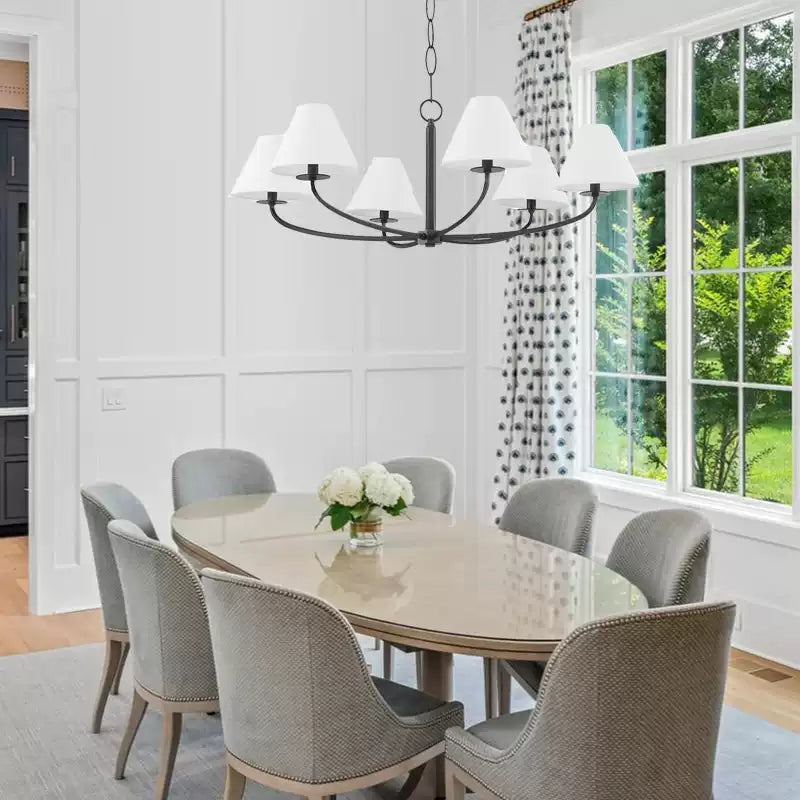 White-shade Stacey black chandelier above rounded dining table and grey chairs beside large window and patterned curtain