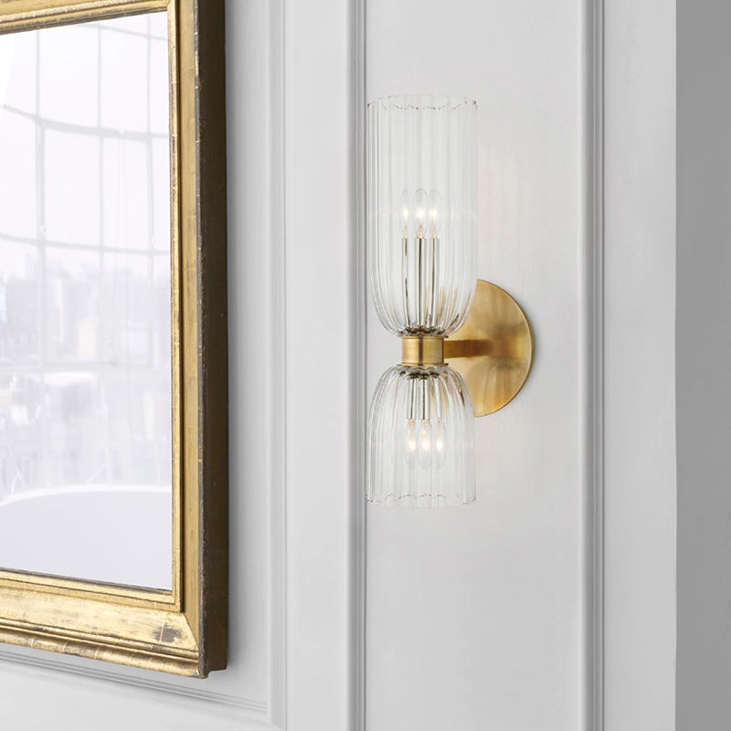 Close view of glowing double ribbed glass cups and brass-tone collar beside a gold-framed mirror