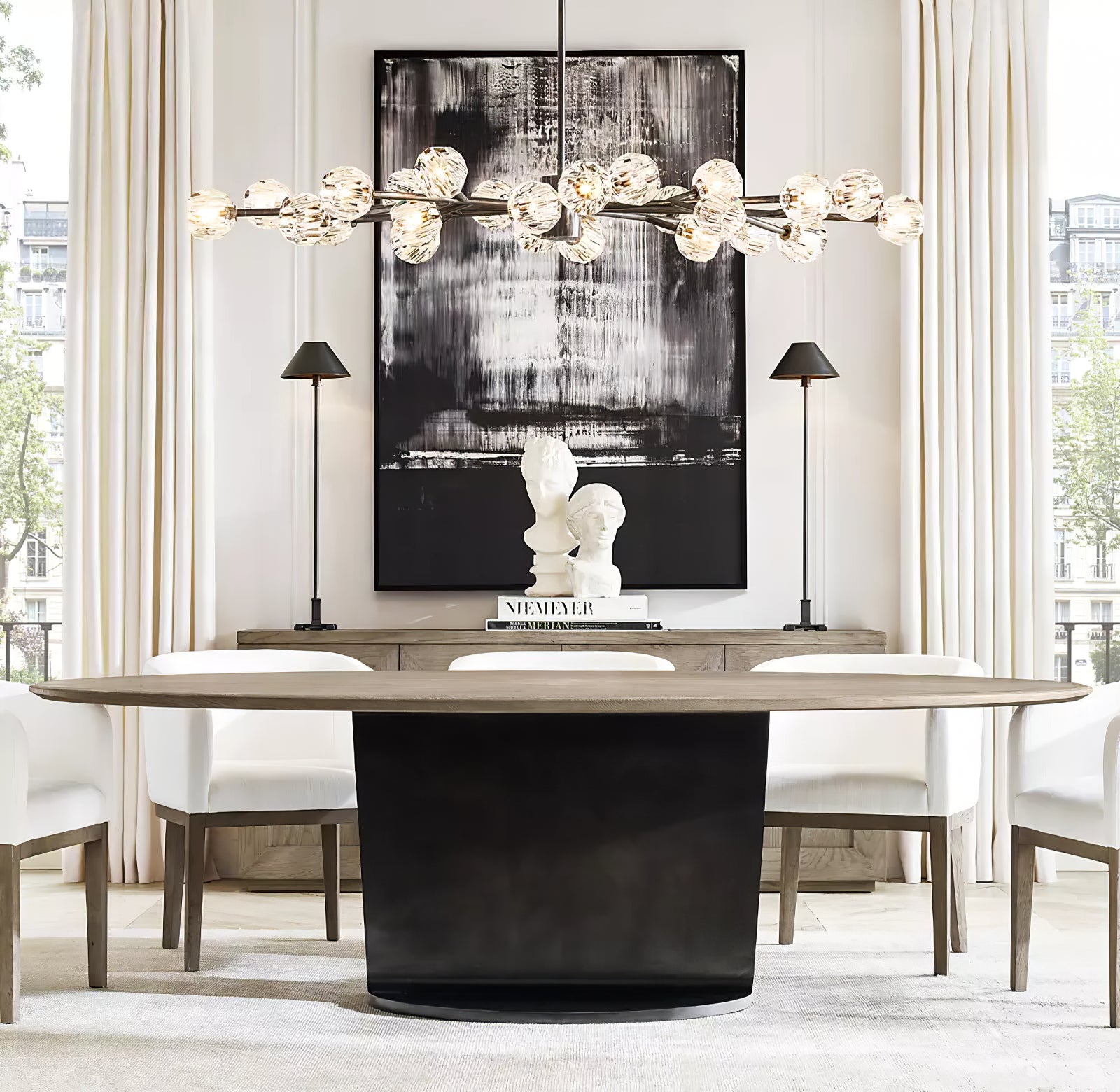 Two Black B Slim Candlestick lamps with dark shades on sideboard behind dining table beneath separate glass globe chandelier