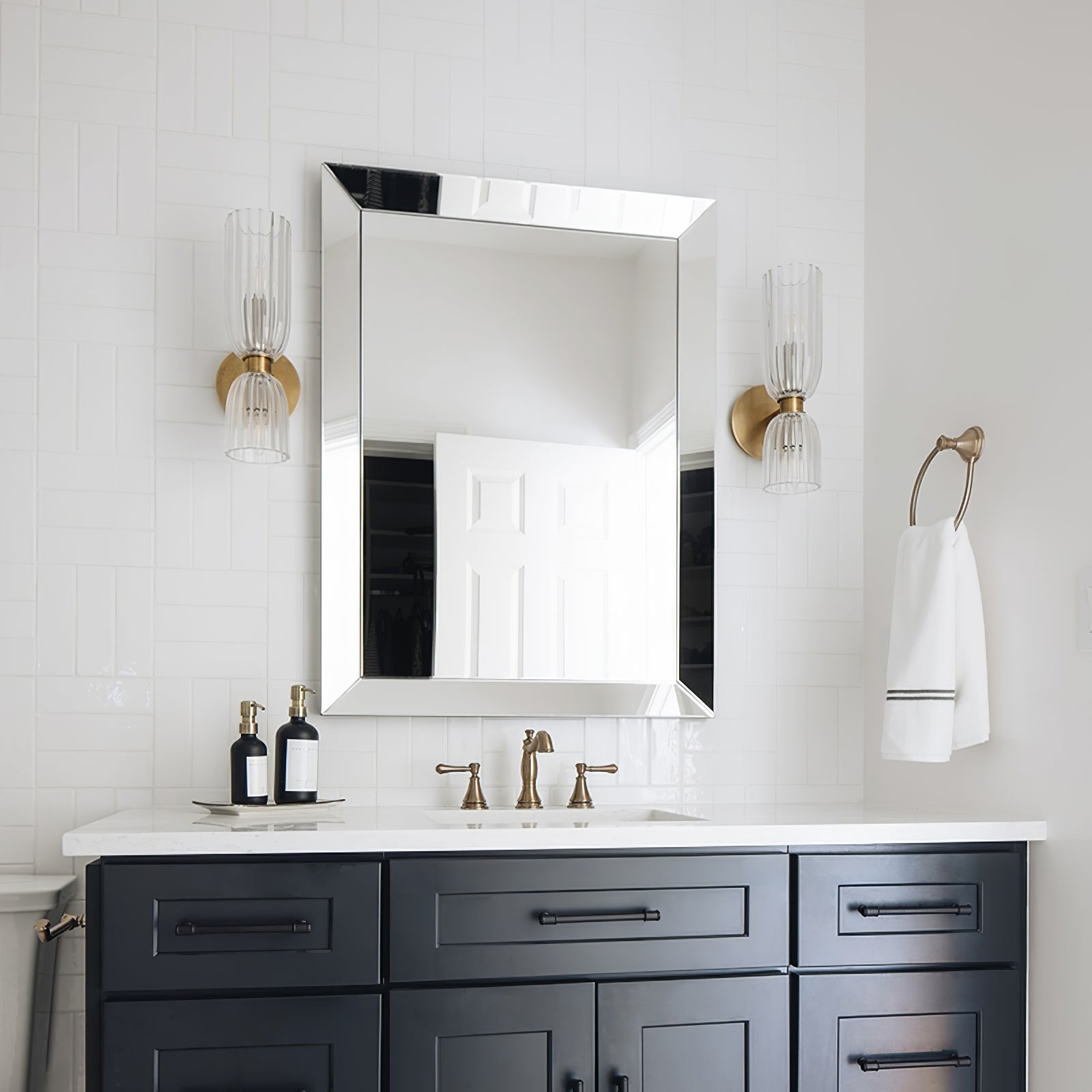 Two Antique Brass-tone double sconces beside a silver-bevelled mirror above a blue vanity against white tiles