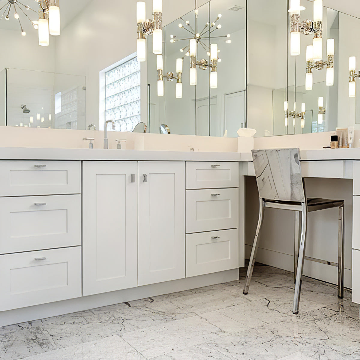 Illuminated silver-tone double cylinder sconces and reflections across mirrored bathroom walls above a white vanity