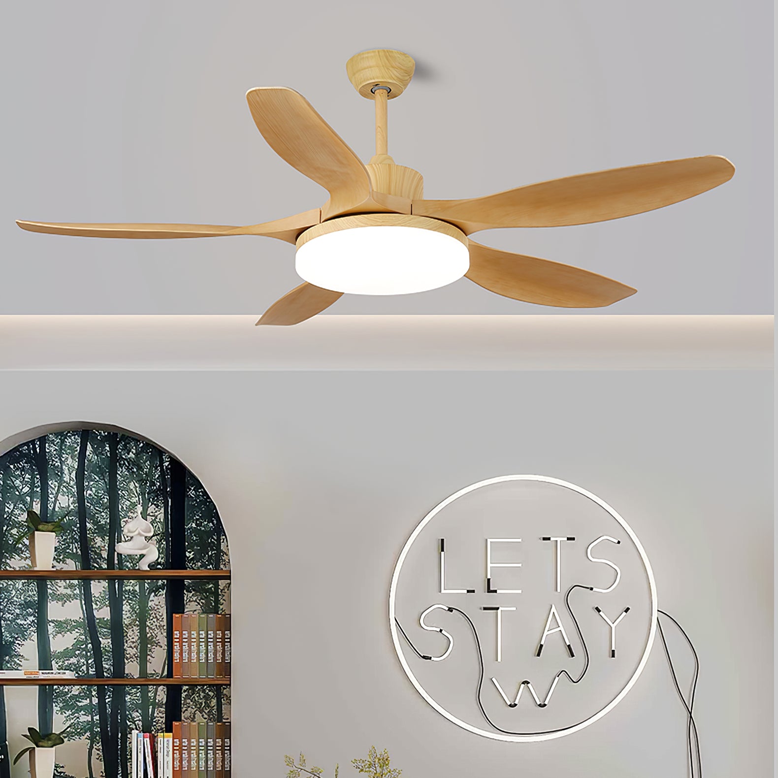 Wood-tone five-blade fan and bright round light above an arched bookcase and circular LETS STAY wall decoration