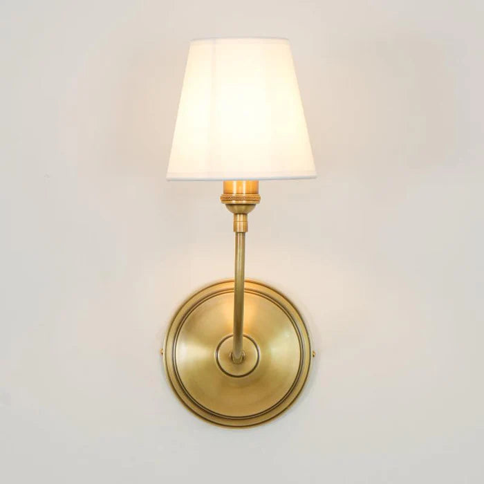 Front wall view of an illuminated brass single A lamp and round backplate.