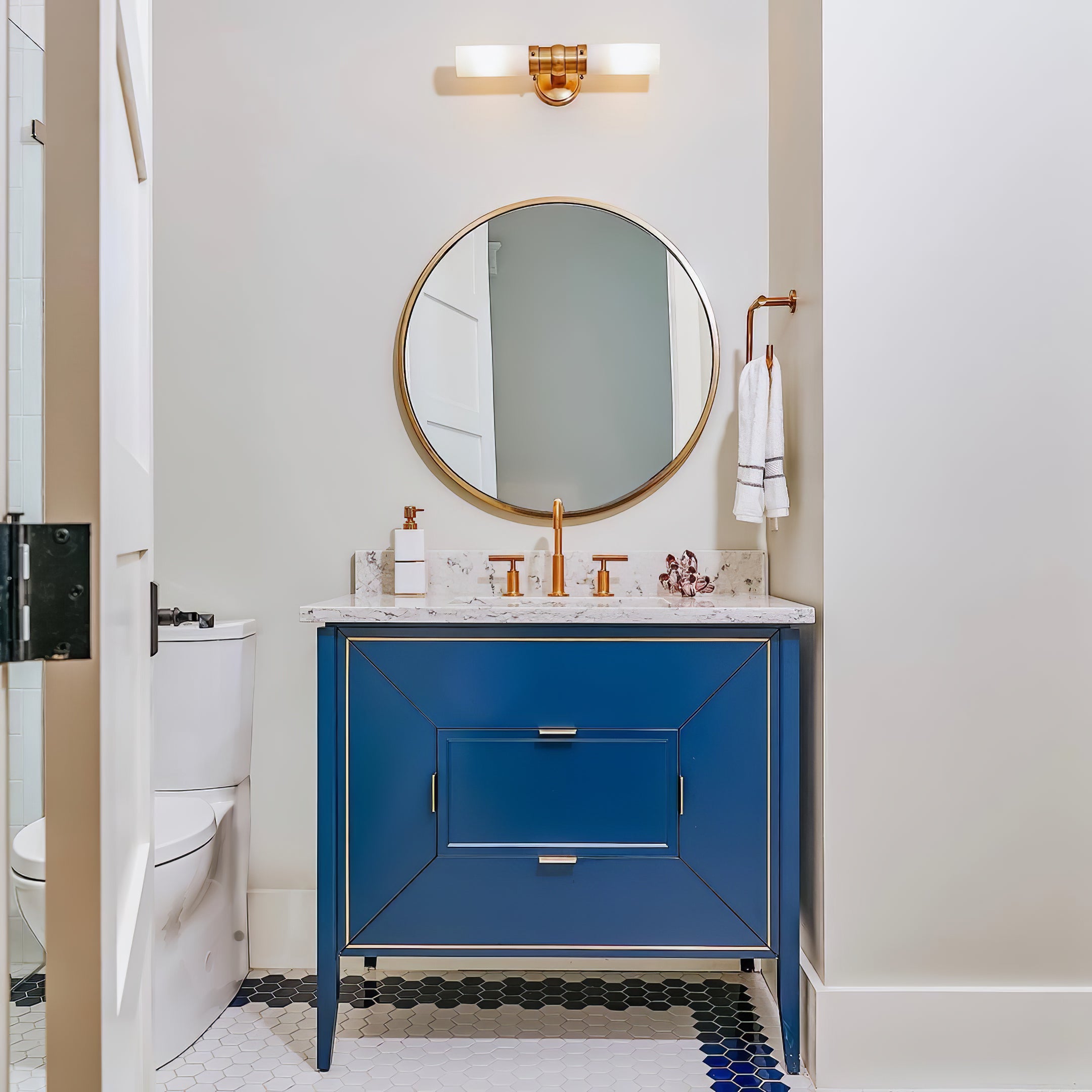 Brass-tone double white-glass wall light mounted horizontally above a round mirror and blue bathroom vanity