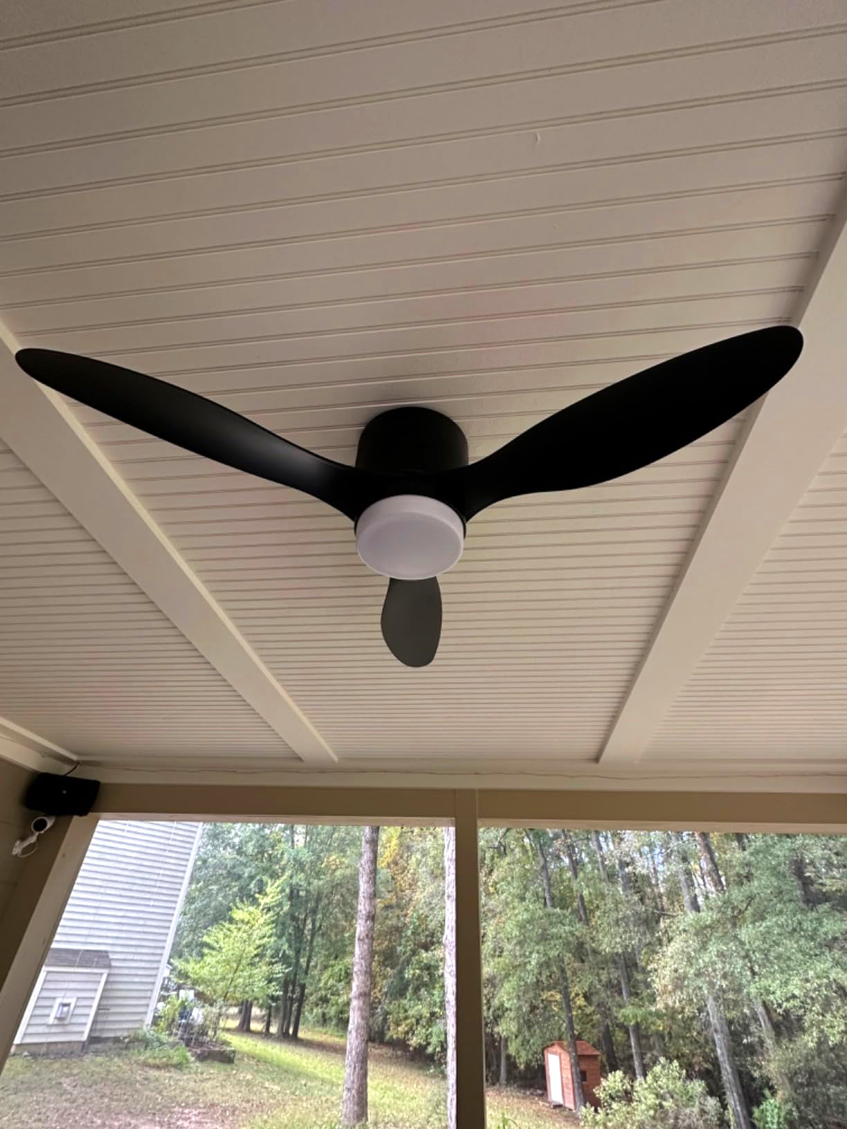 Black fan photographed beneath a wooden porch roof