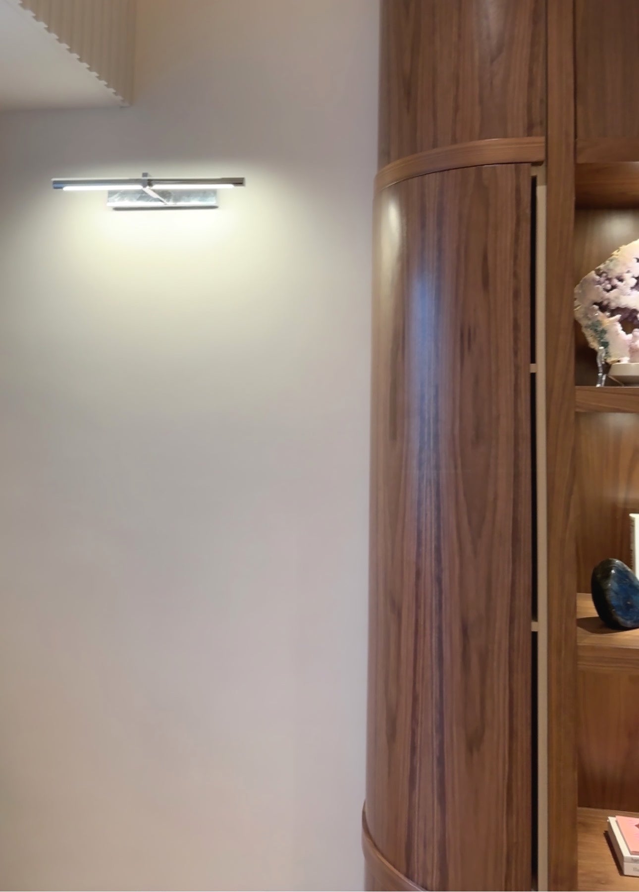 Lit silver-colour picture light on a pale wall beside curved wooden display shelving